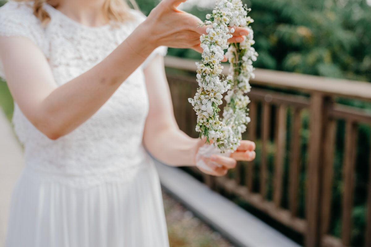 Braut reicht Haarkranz aus weißen Blumen