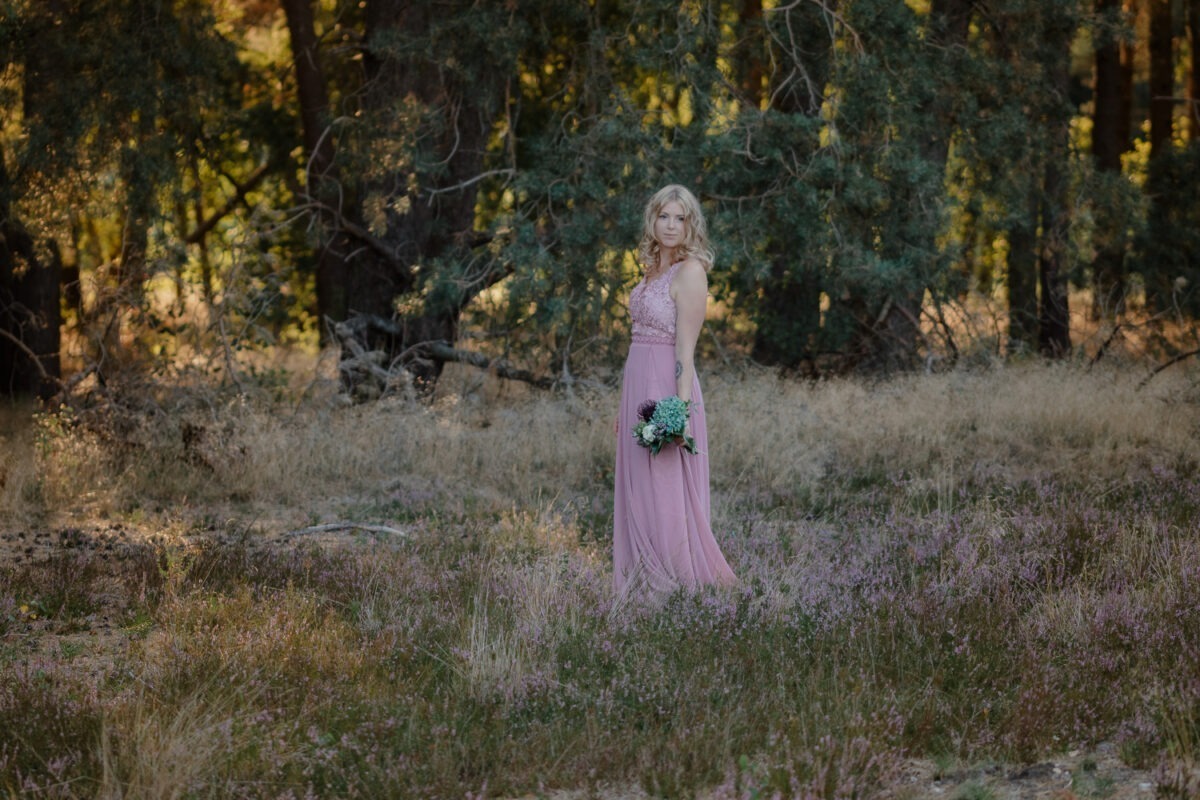 Frau mit rosa Kleid in der Verdener Heide im Sonnenuntergang, an Kamera vorbeischauend