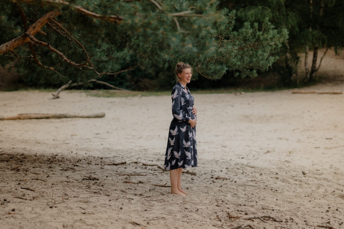 Schwangerschaftsfotografin in Bremen: Unvergessliche Momente festhalten 5 Porträtaufnahme, Babybauch, Schwangere Frau lachend in den Dünen, Wald im Hintergrund