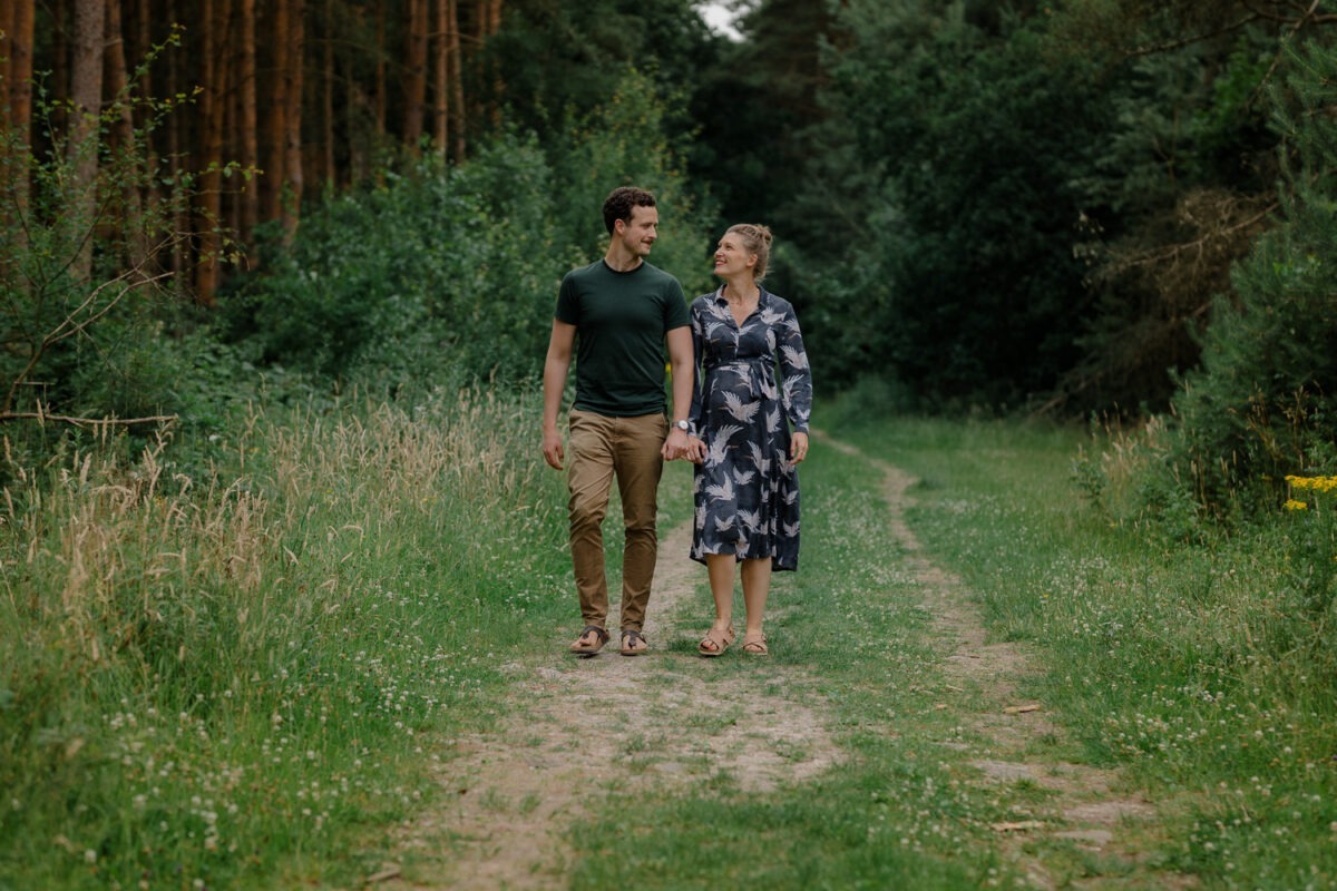 Schwangerschaftsfotografin in Bremen: Unvergessliche Momente festhalten 6 Paarfoto, Paar laufend im Wald, Frau mit Babybauch, Mann schaut Frau an