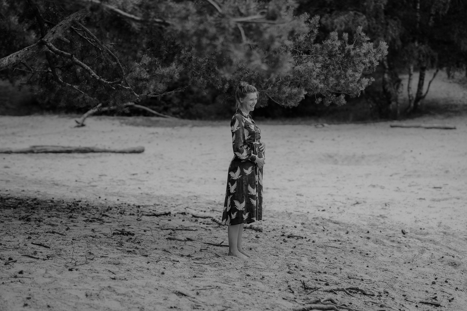 Schwangerschaftsfotografin in Bremen: Unvergessliche Momente festhalten 1 Schwarz-Weiss Aufnahme, Babybauch, Schwangere Frau lachend in den Dünen, Wald im Hintergrund