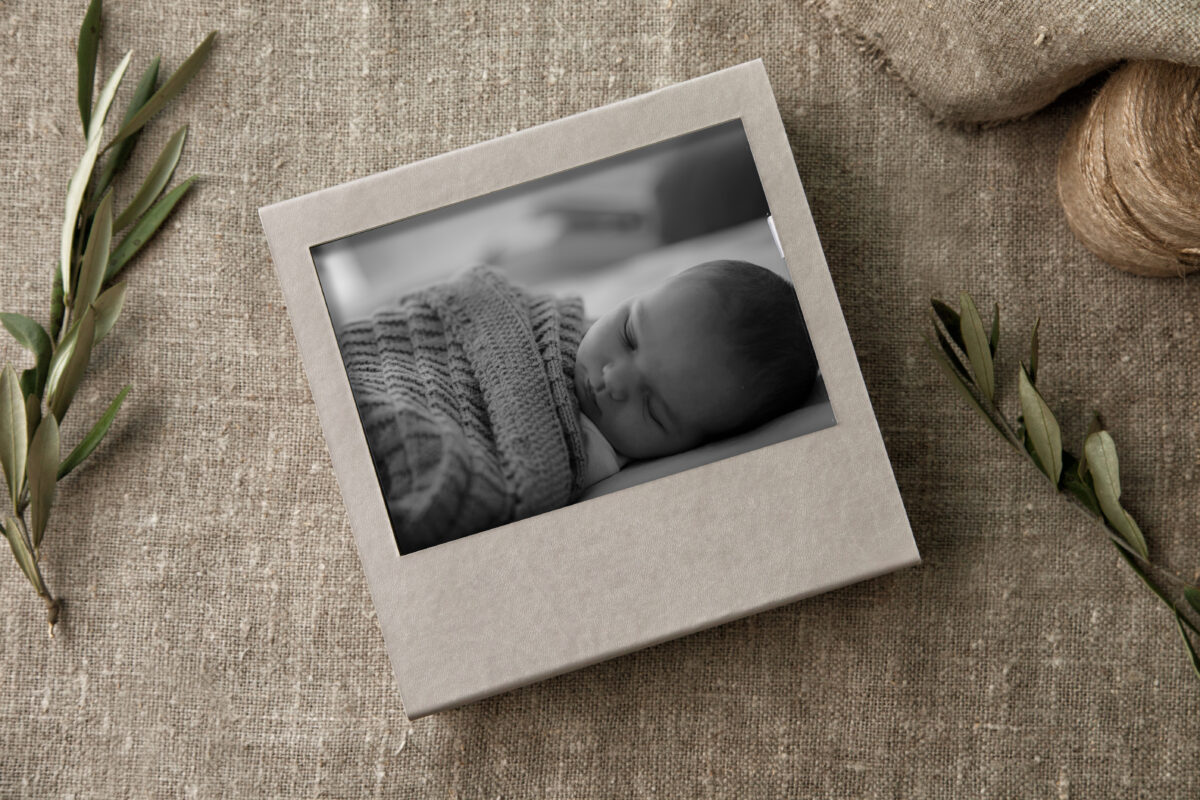 Ein Schwarz-Weiß-Foto eines schlafenden Babys in einer Fotokiste aus Kunstleder, aufgenommen von einem Bremer Familienfotografen. Amavi Hochzeits- und Familienfotografie