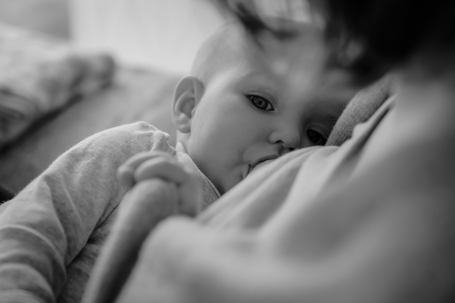 Stillfoto von Mutter mit Baby in schwarz-weiss, Baby schaut in die Kamera während es trinkt