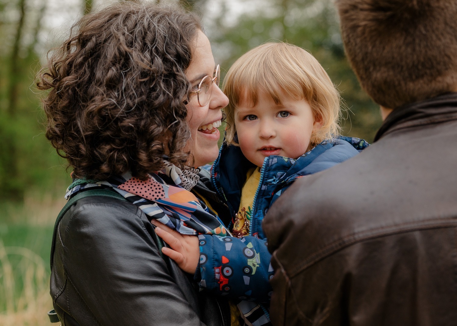 Familienreportagen, Familienfotografie, Familienfoto mit Mutter, Vater und Tochter, Kind schaut in Kamera, Eltern schauen zur Seite