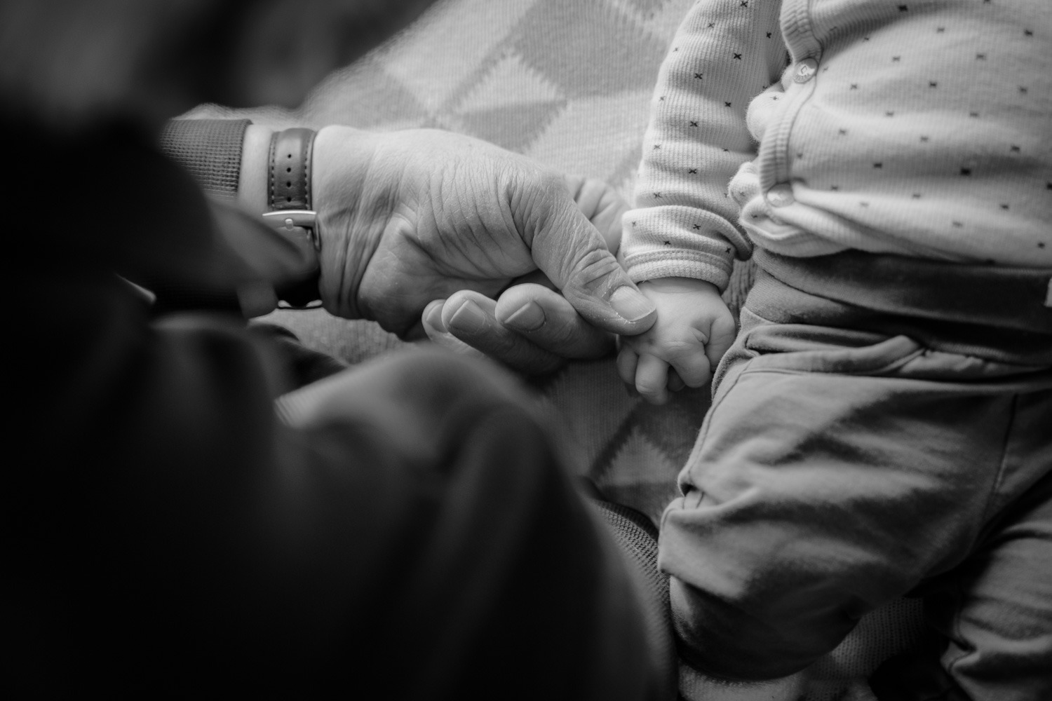 Schwarz-weiss Detailfoto von altem Mann der Babyhand hält