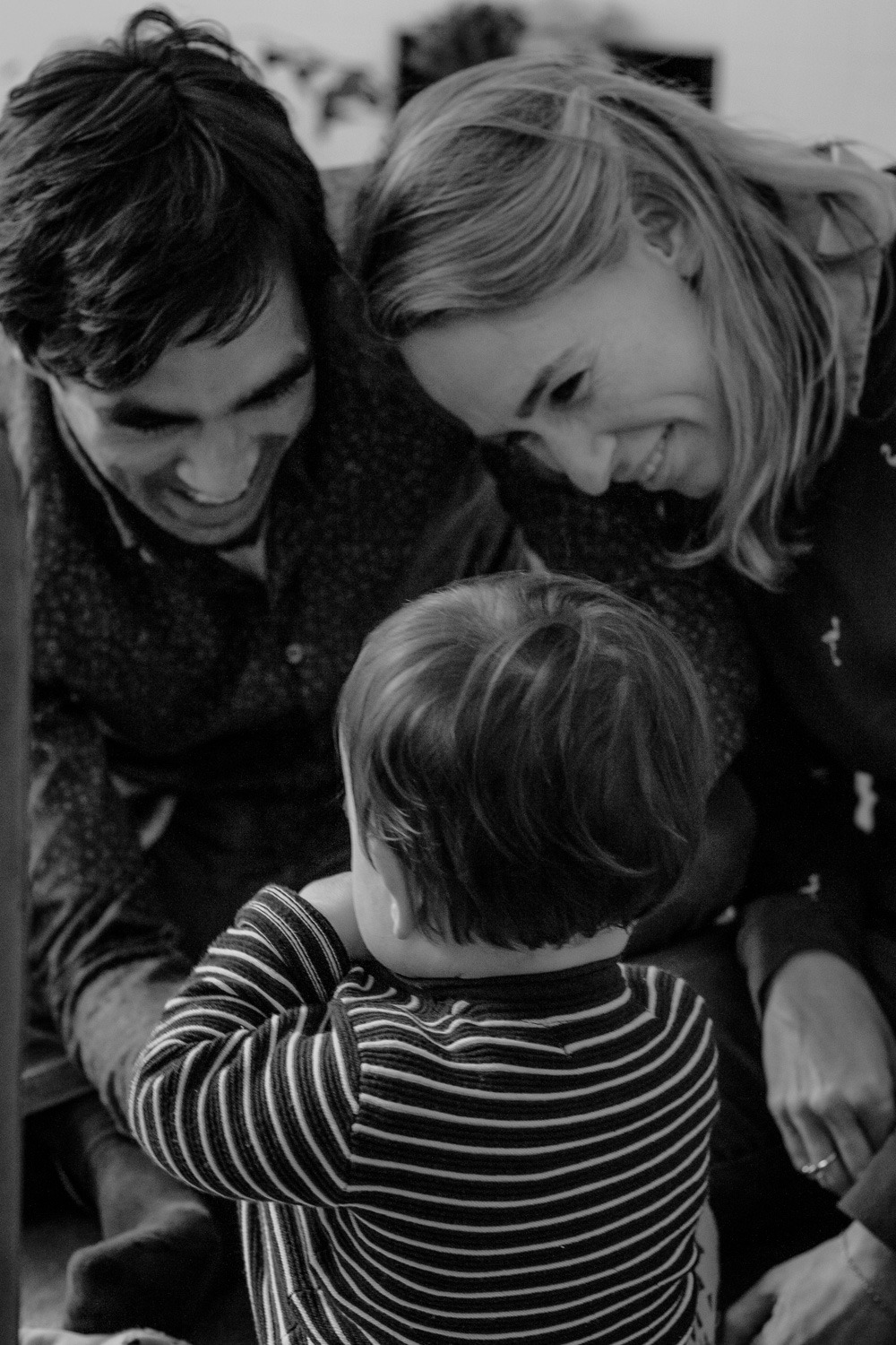 Schwarz-Weiss Familienfoto mit Eltern die ihr Kind lachend anschauen, Kind mit Rücken zur Kamera