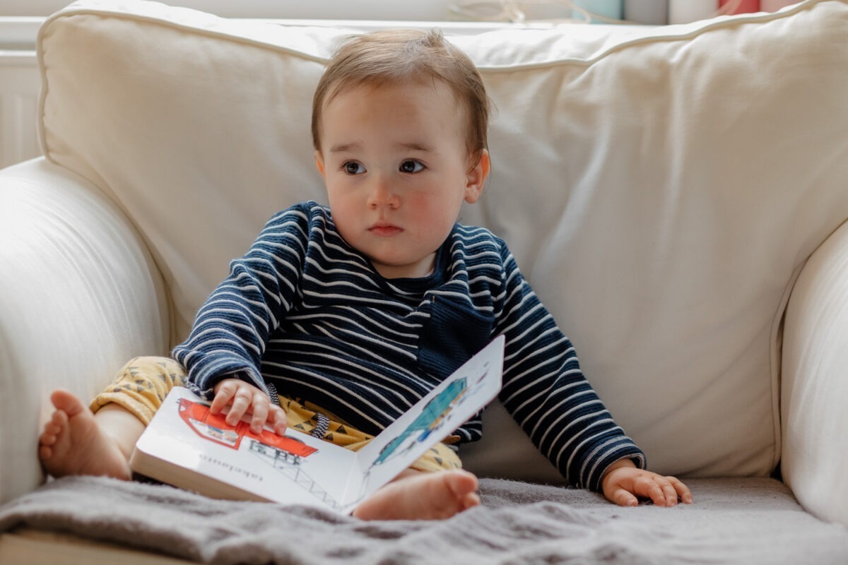 Homestory, kleiner Junge sitzt in großem weißen Sessel und schaut in ein Buch