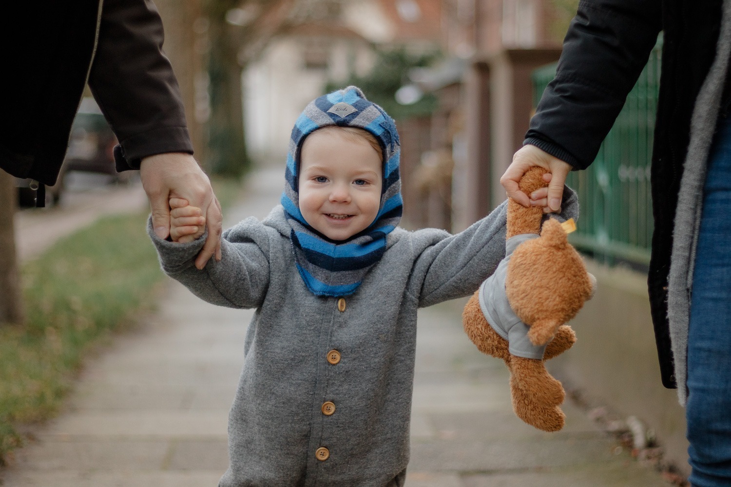 Familienfoto mit Kind in der Mitte, in Kamera schauend und Teddy haltend