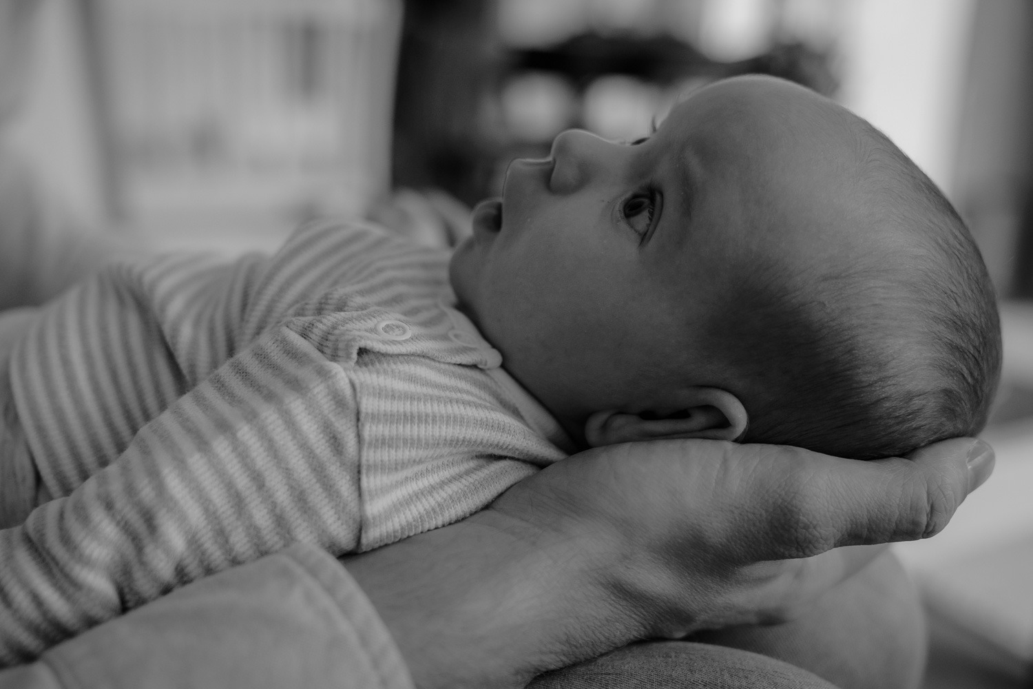 Schwarz-Weiss Momentaufnahme von Baby, liegt in geöffneter Männerhand und schaut Vater an