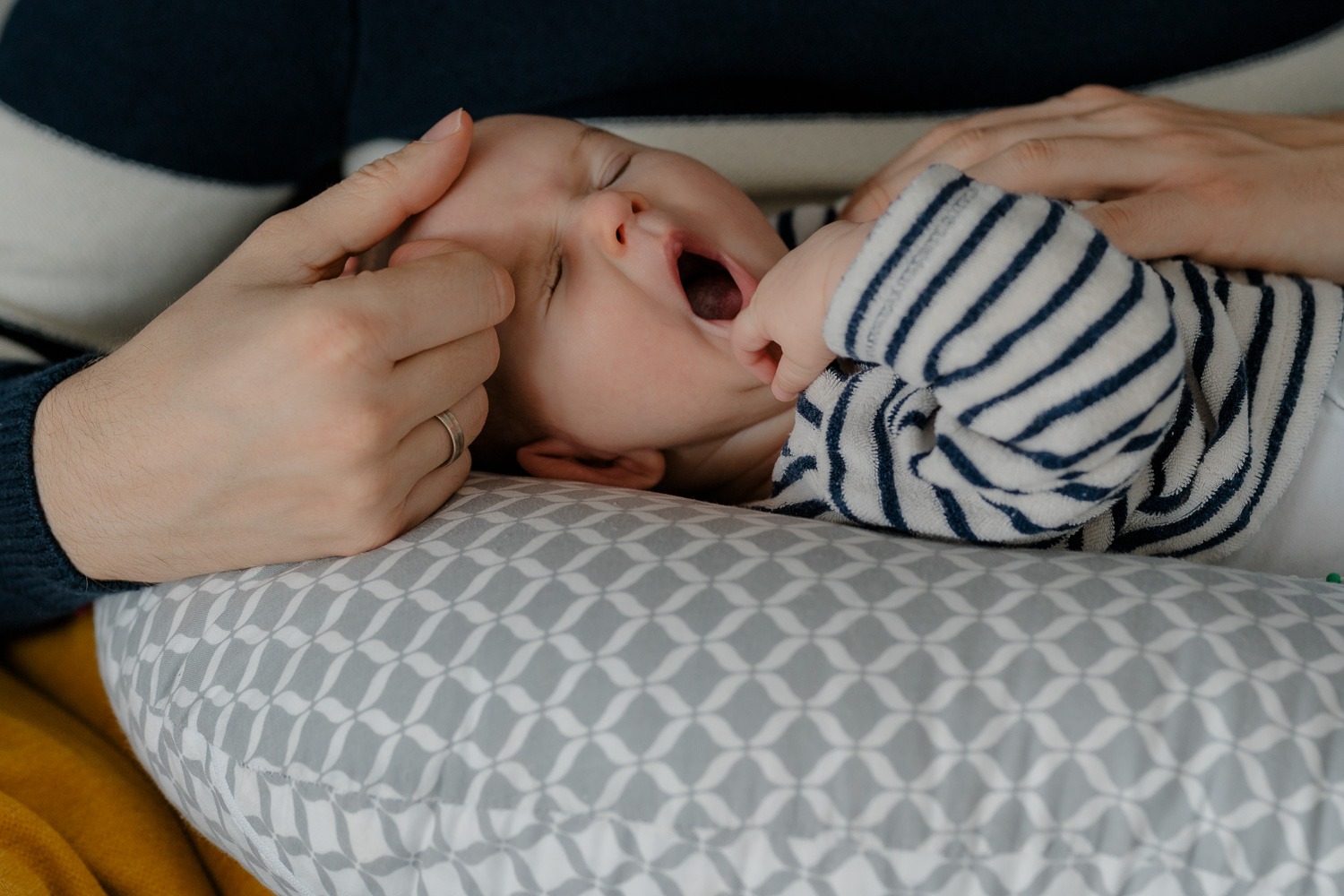 Baby auf Stillkissen von Männerhänden gehalten während Baby gähnt