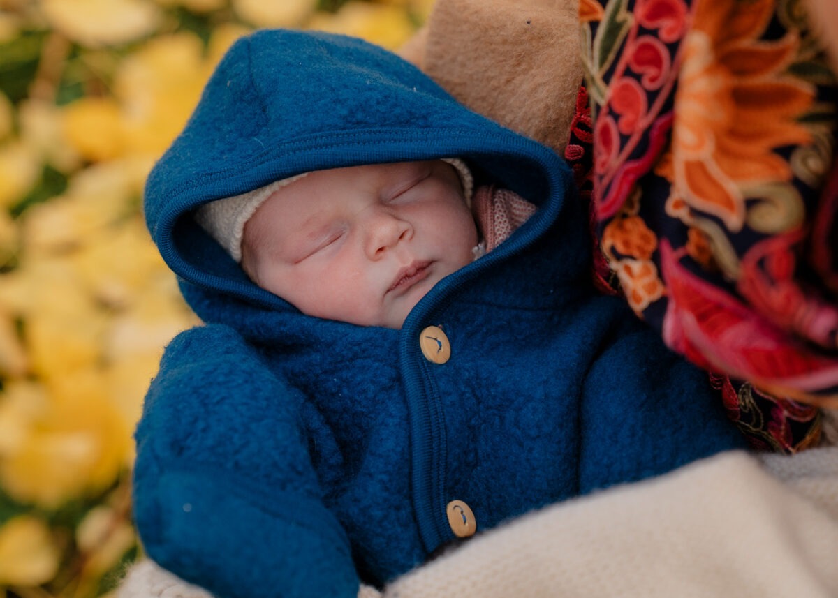 Porträtaufnahme von schlafendem Baby in blaunem Wollwalkanzug