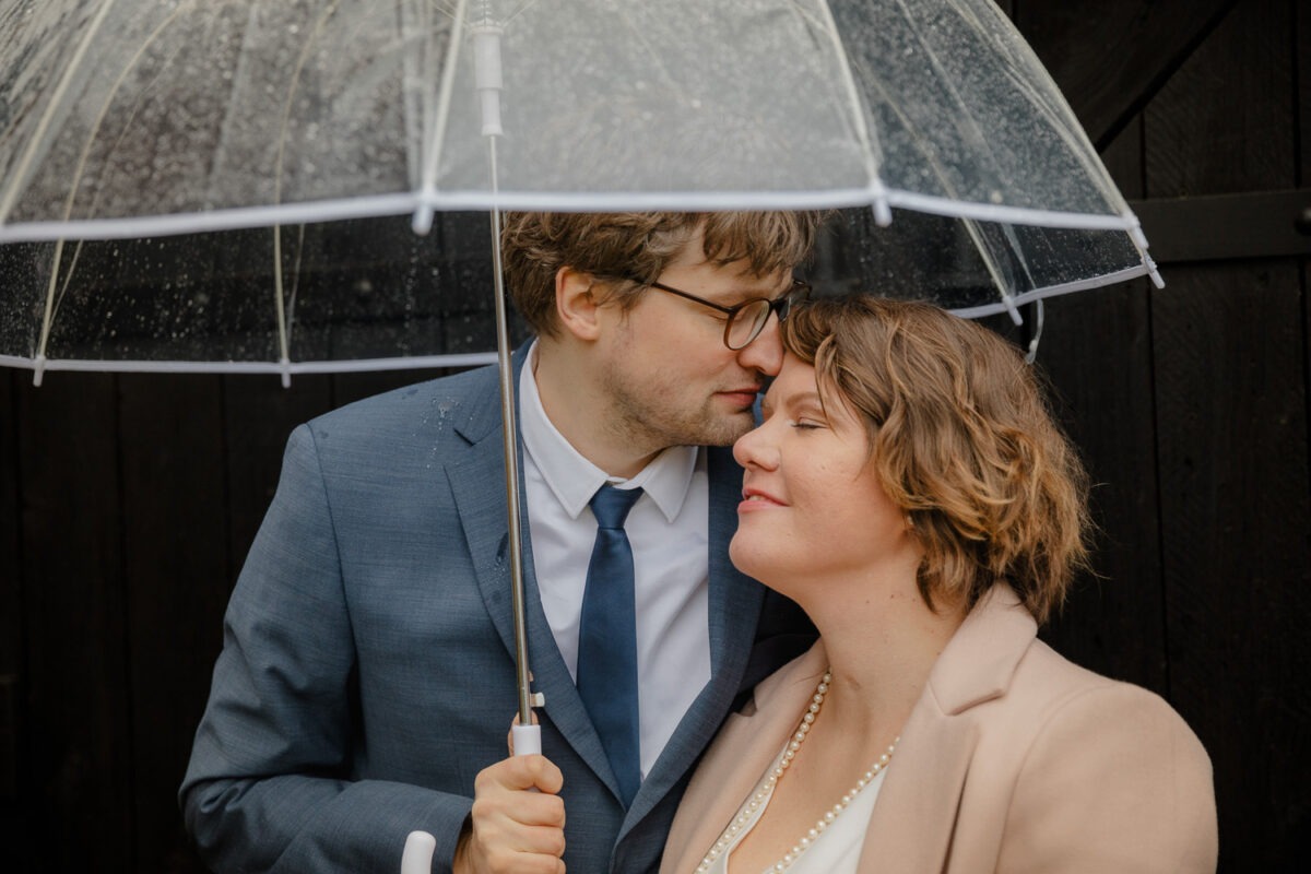 Bräutigam küsst Braut unter durchsichtigem Regenschirm während Brautpaarshooting