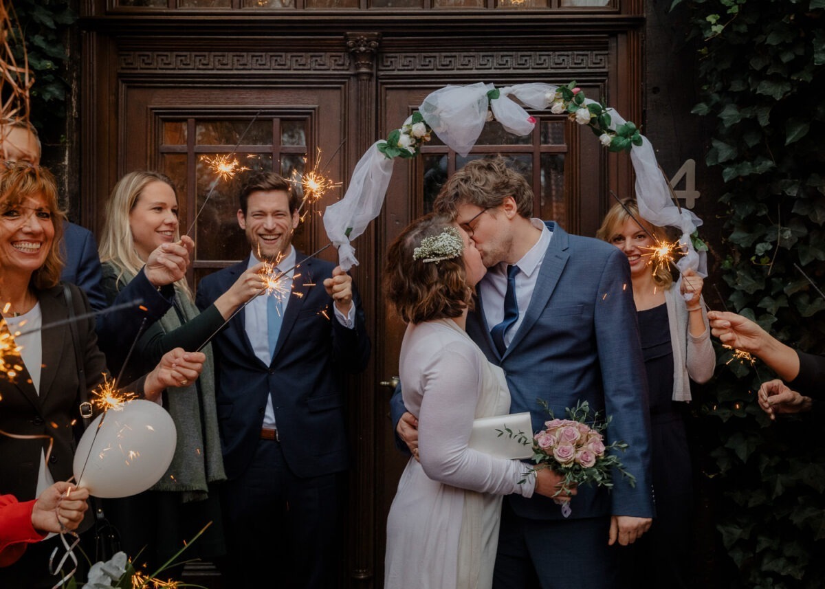 Hochzeitsfotografin Worpswede 2 Brautpaar küssend umringt von Wunderkerzen und Gästen vor dem Standesamt Gut Varrel in Niedersachsen