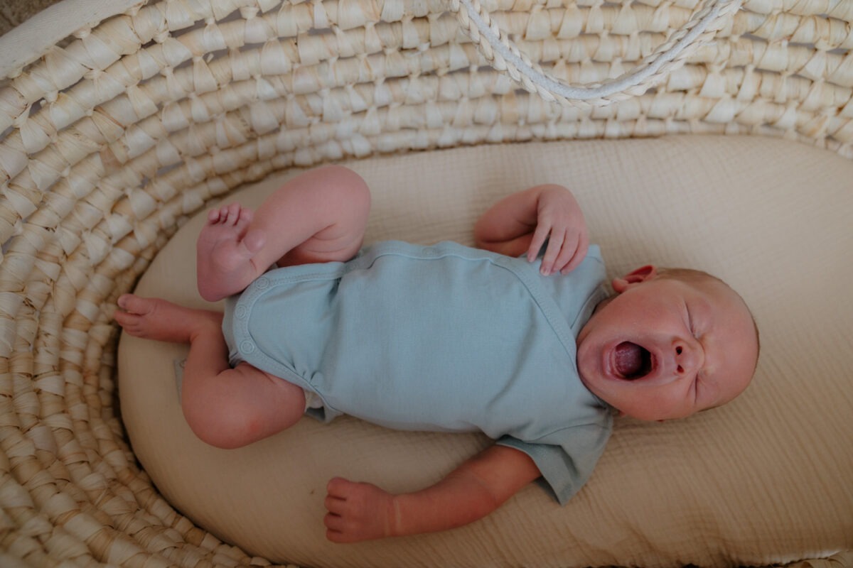 Babyfoto von oben herab fotografiert, Baby gähnend in Körbchen liegend mit hellblauem Body