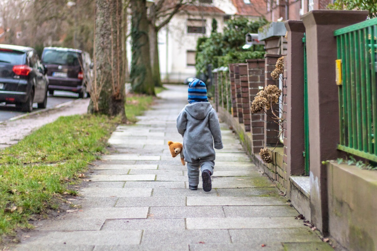 Kleinkind mit Teddy läuft von Kamera weg
