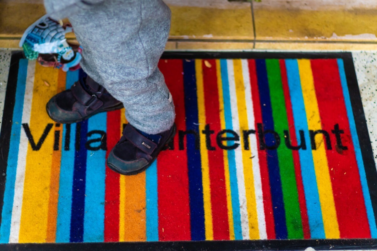 Detailaufnahme Kind stehend auf bunten Abtreter mit den Worten "Villa Kunterbunt"