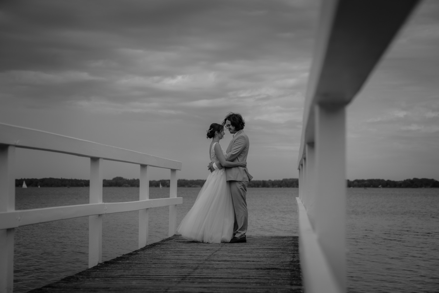 Schwarz-Weiss, Brautpaar umarmend, einander zugewandt auf Brücke am Bad Zwischenahner Meer